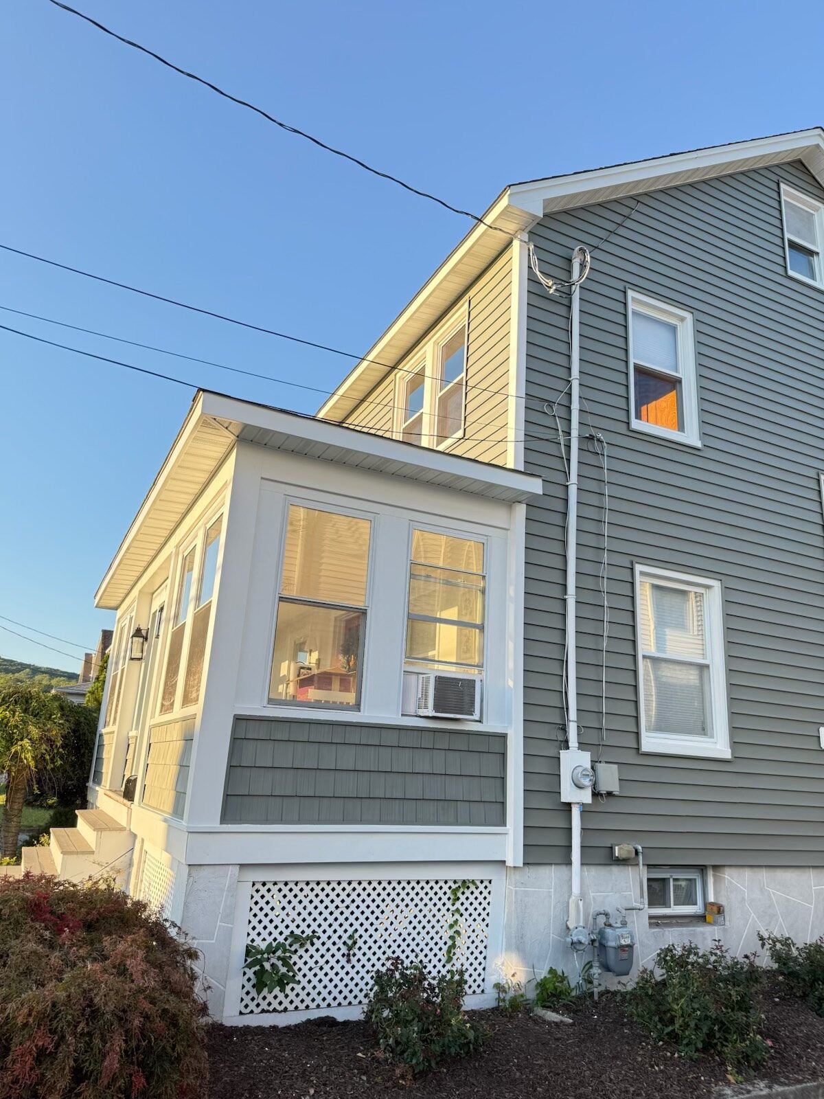 Side view of a two-story house with a porch. Gray siding, white trim, and a blue sky.
