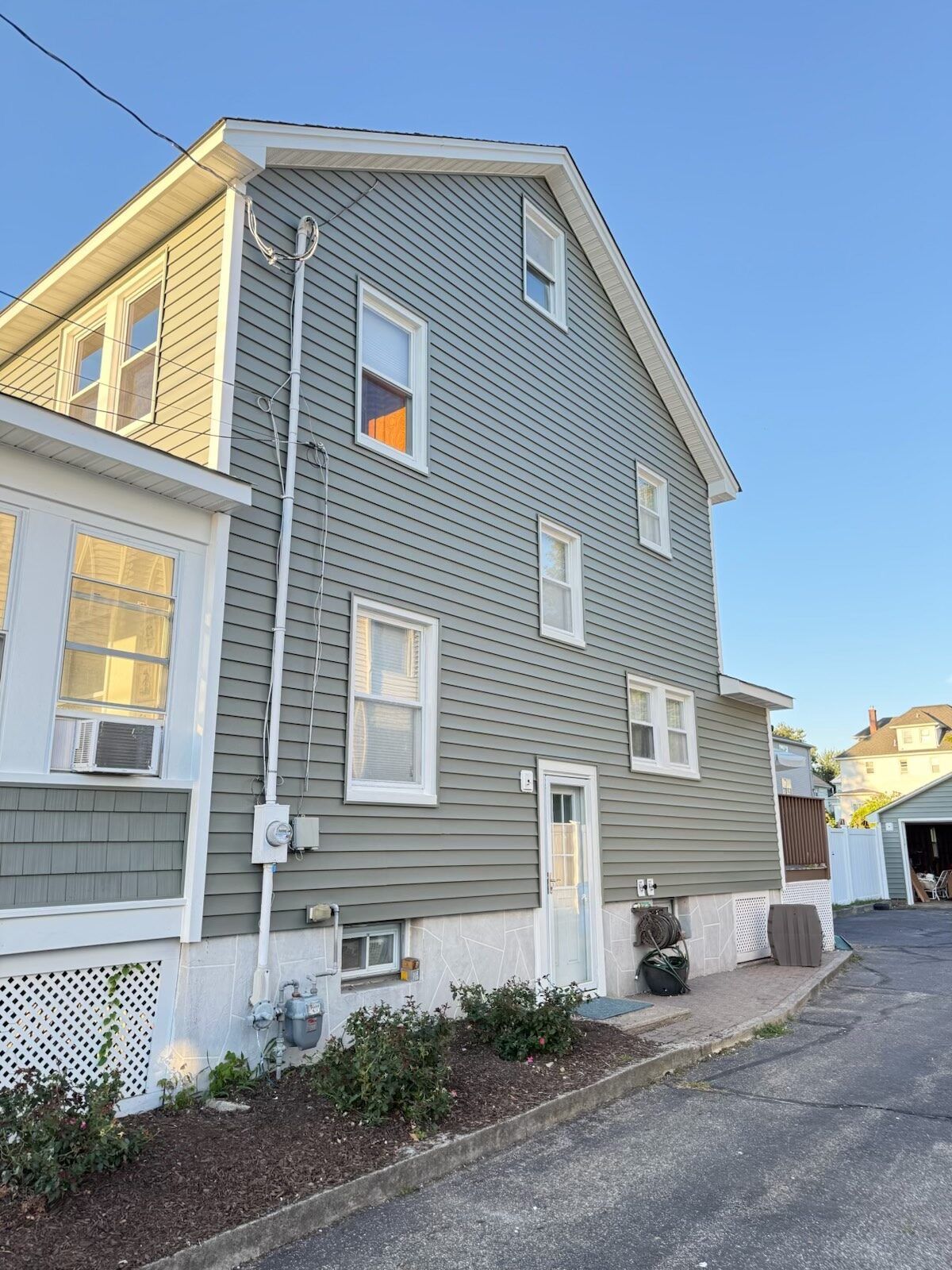 Two-story house with light green siding and white trim. Windows and door. Pathway along the side.