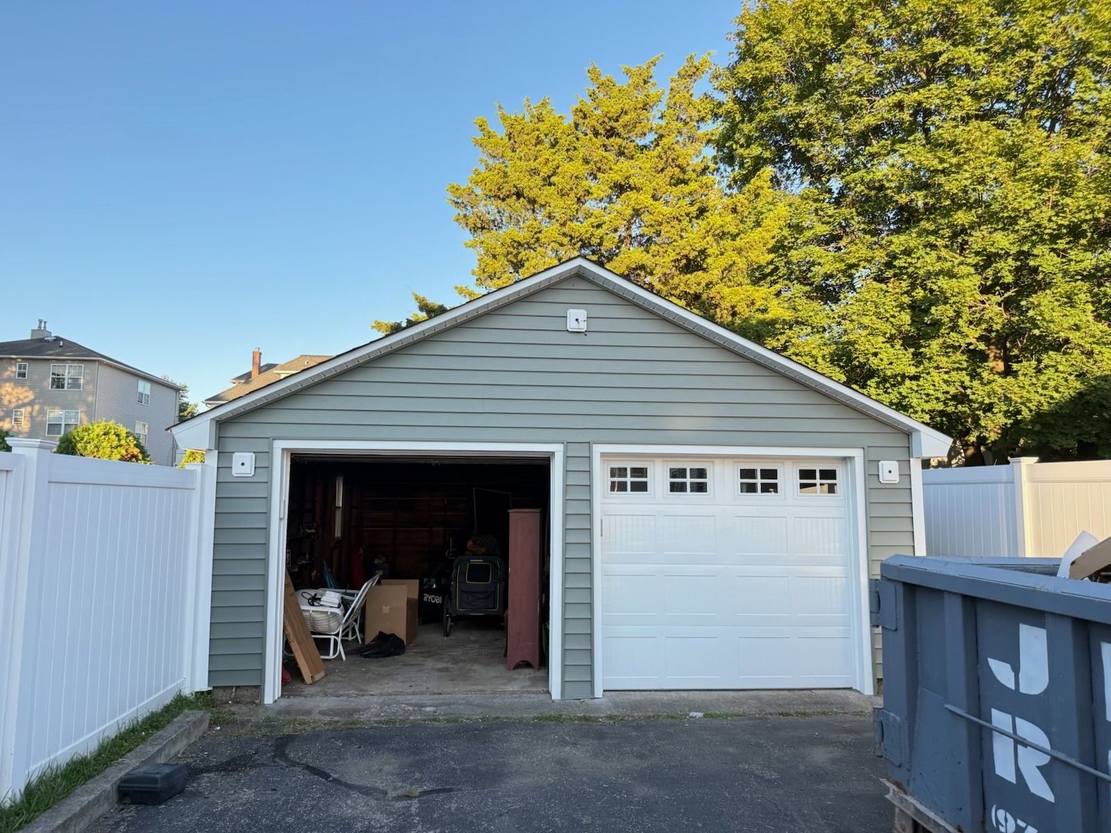 Two-car garage with one open bay showing contents. Green siding, white trim and garage door, blue sky.