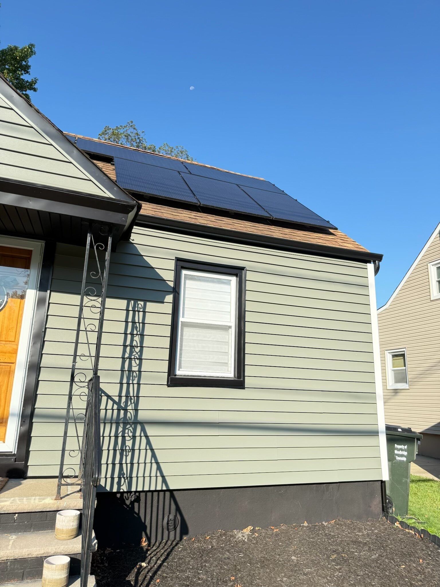 Solar panels on a light green house with a black window frame, blue sky.