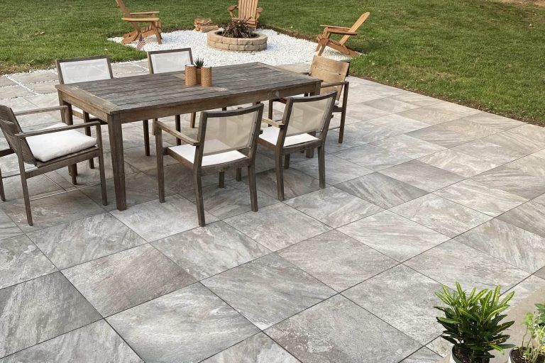 Patio with gray stone tiles, a wooden table, and chairs. Fire pit and grass in the background.
