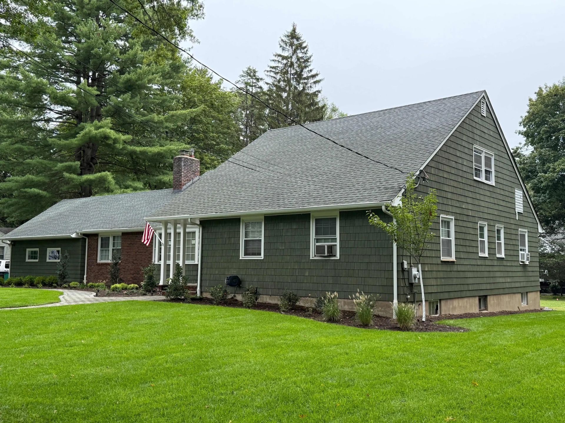 House with gray roof, small window, and brick chimney; trees in the background. Overcast sky.