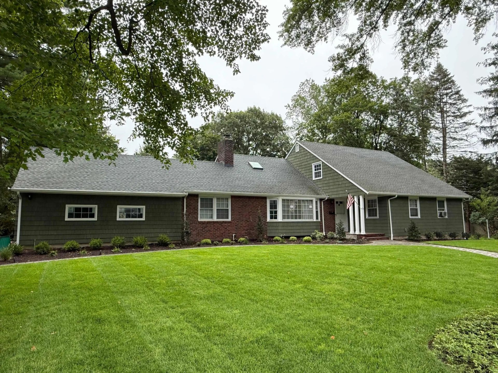 Green house with brick facade and manicured lawn.