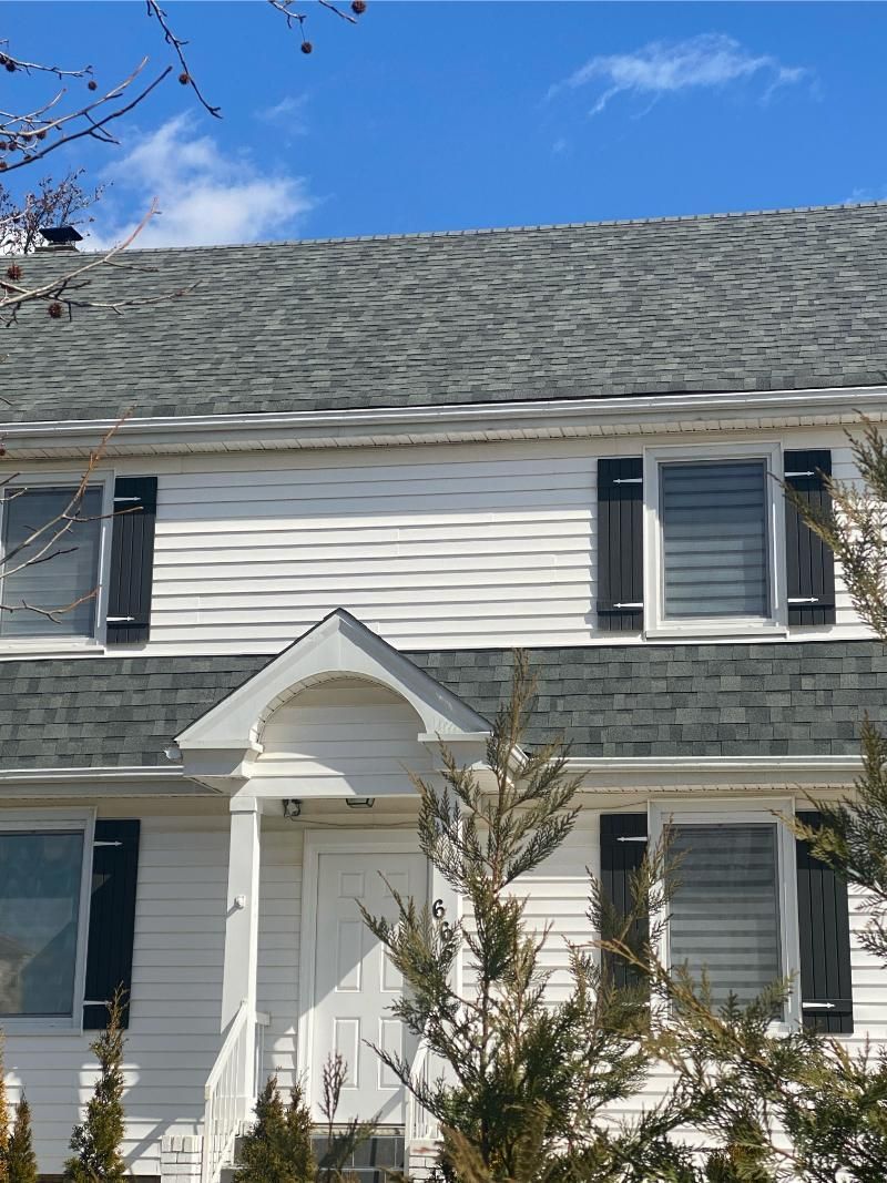 White house with gray roof, black shutters, and blue sky.