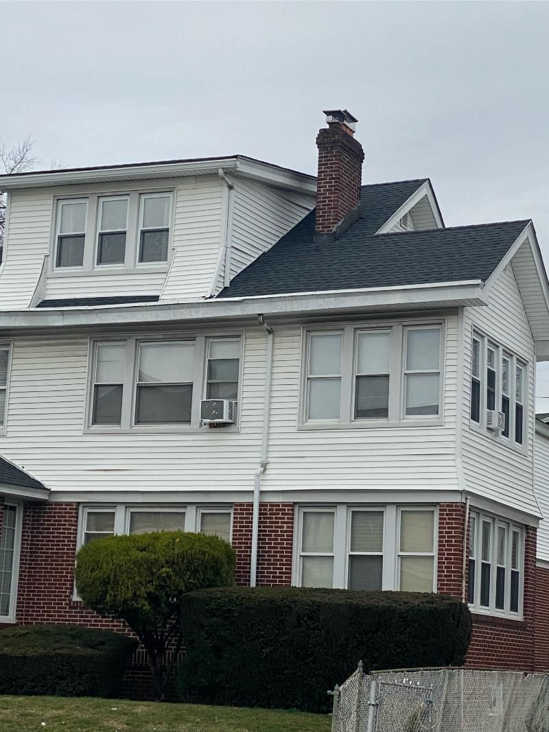 Multi-story house with brick base, white siding, multiple windows, and a chimney on a cloudy day.
