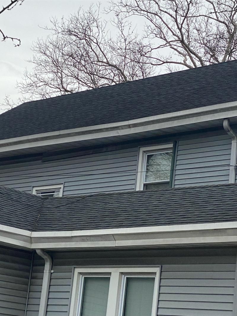Gray house with gray roof, white trim, and leafless tree branches overhead.