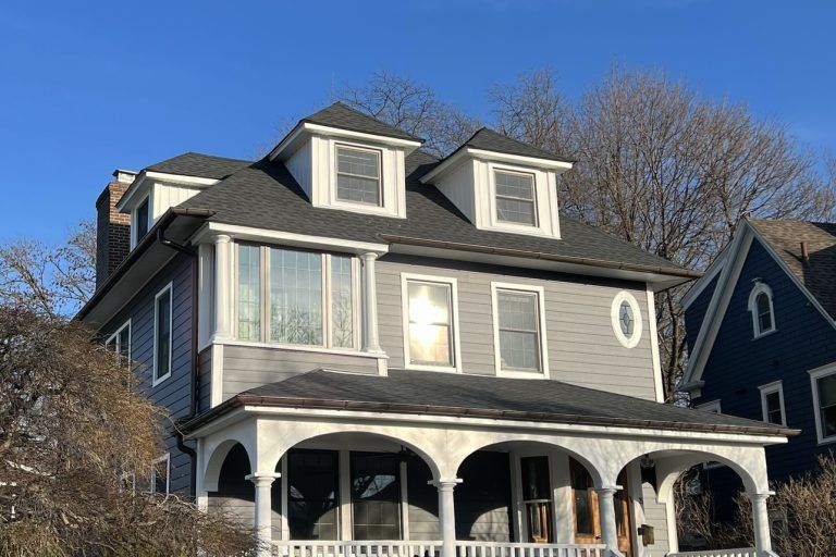 Two-story gray house with porch and dormers on a sunny day.