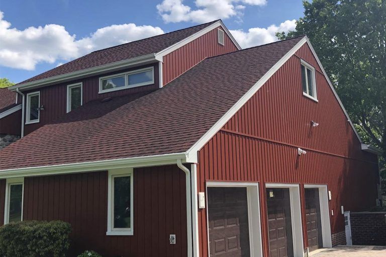Red house with brown roof and white trim under a blue sky with fluffy clouds.