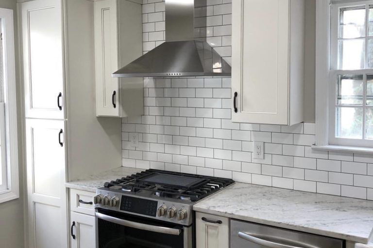 Kitchen with white cabinets, stainless steel stove and range hood, and white subway tile backsplash.