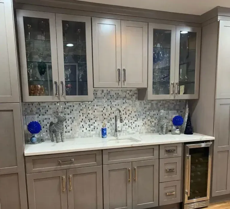 Gray cabinetry with glass-front uppers, white countertop, mosaic backsplash, and wine cooler.