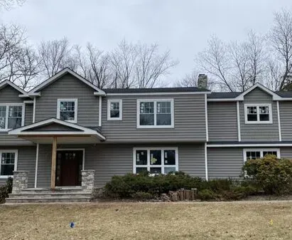 Gray house with white-trimmed windows and stone porch, under a gray sky.