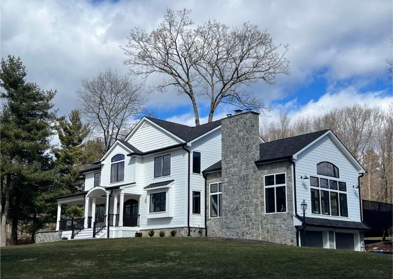 White house with dark roof and stone chimney under a cloudy sky.