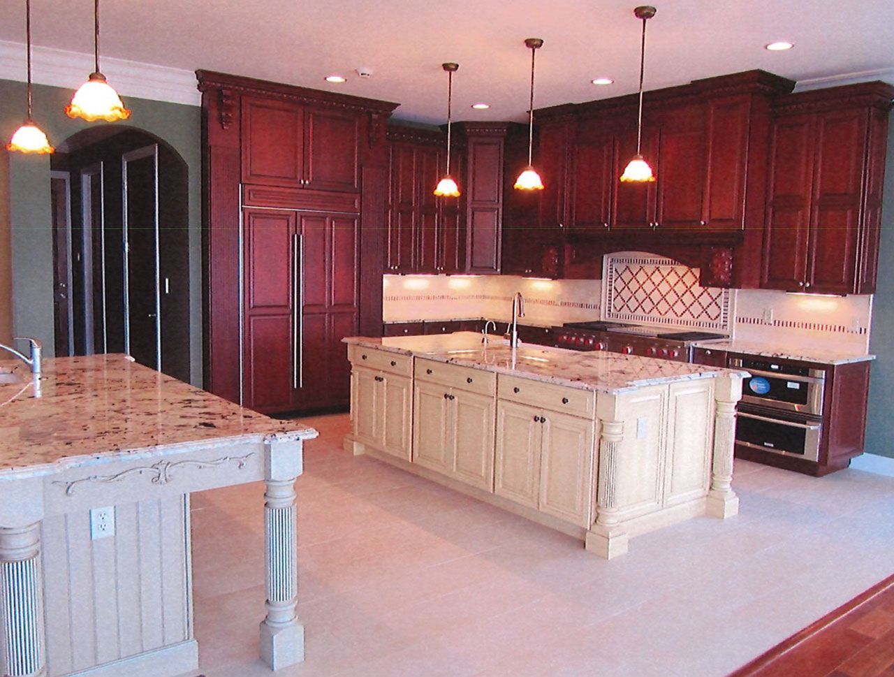 Luxurious kitchen with two islands, dark wood cabinets, light countertops, and pendant lights.