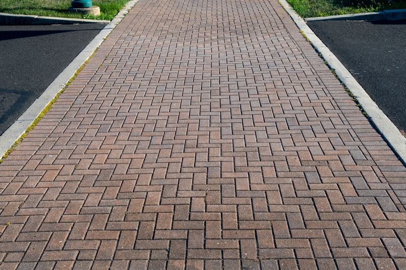Brick walkway between two asphalt areas.