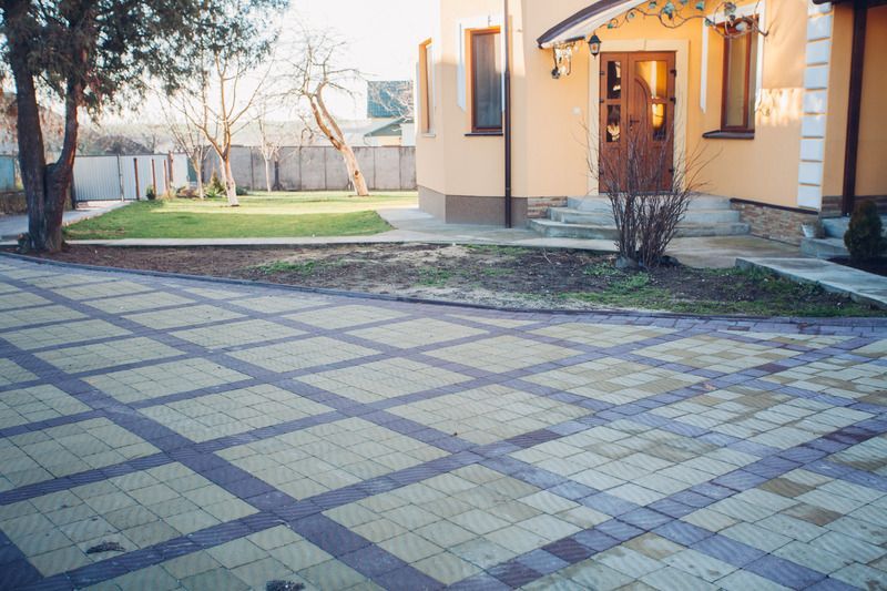 Yellow house with checkered driveway, lawn, and bare trees.