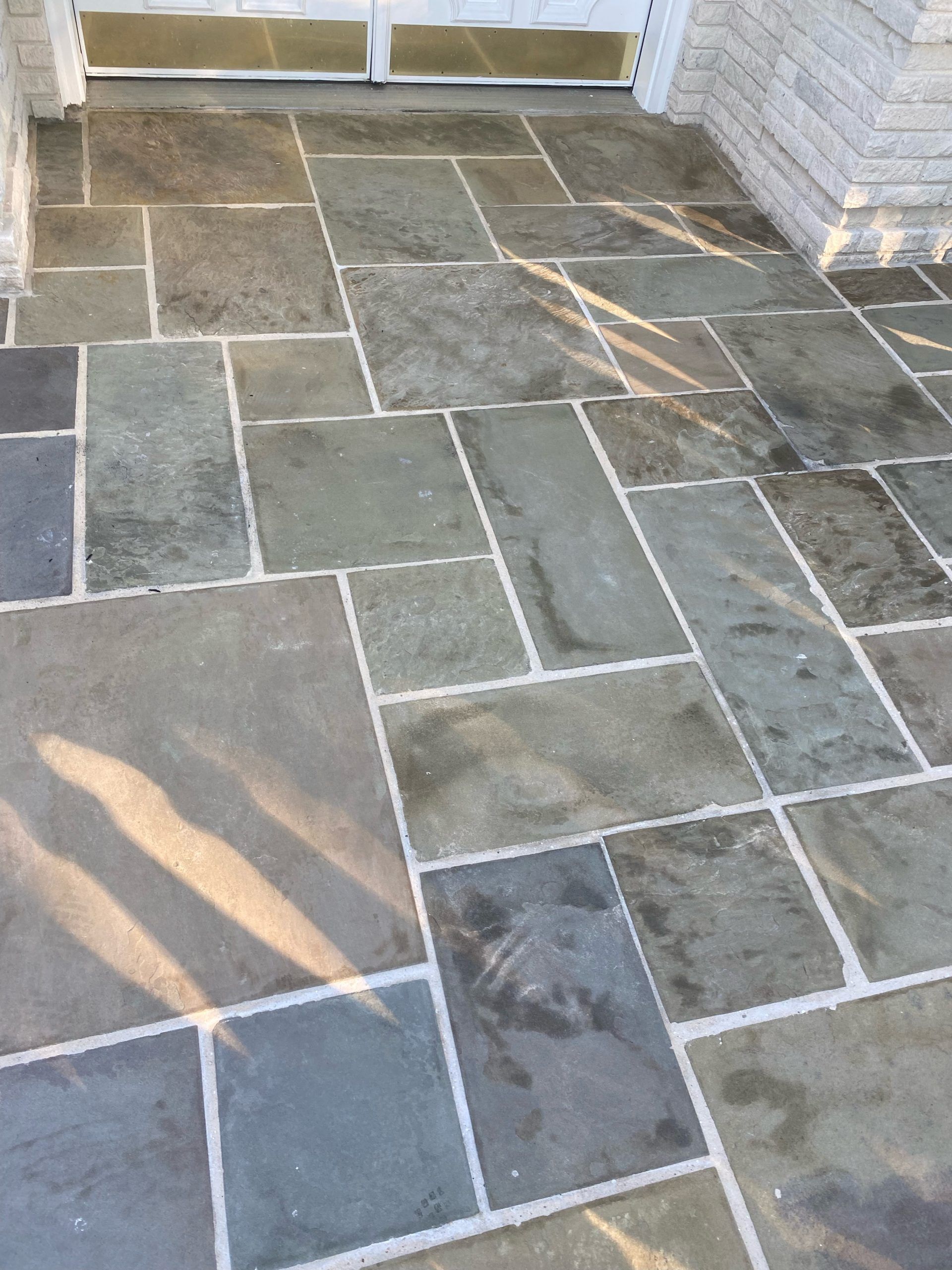 Gray stone patio tiles with white grout, leading to a doorway.