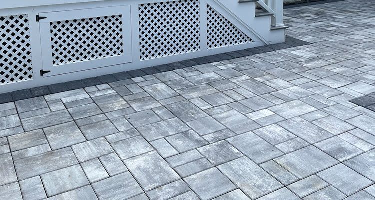 Grey stone patio pavers under a white deck with lattice detailing.