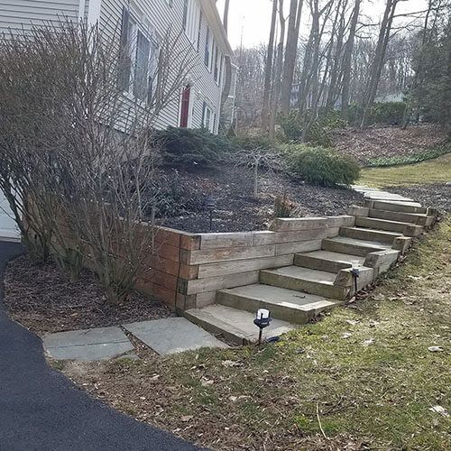 A house with a staircase made of wooden planks and concrete steps leading to the upper level of the yard.