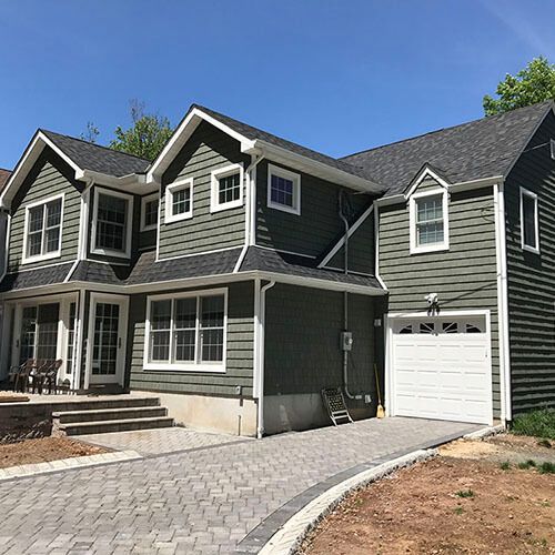 Two-story house with green siding, white trim, and a gray roof; paved driveway and garage.