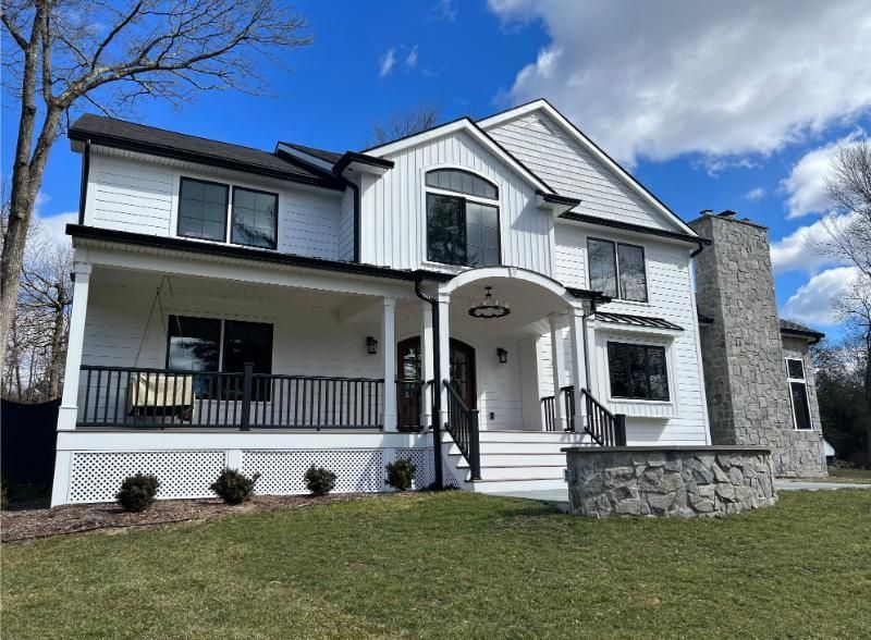 White two-story house with black trim, porch, and a stone chimney.