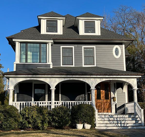 Two-story gray house with white trim, porch, dormers, and brown front door.