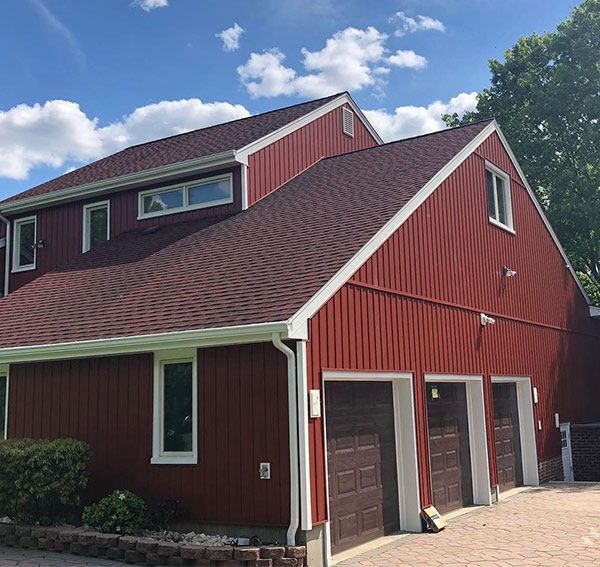 Red two-story house with three-car garage, brown roof, and blue sky.
