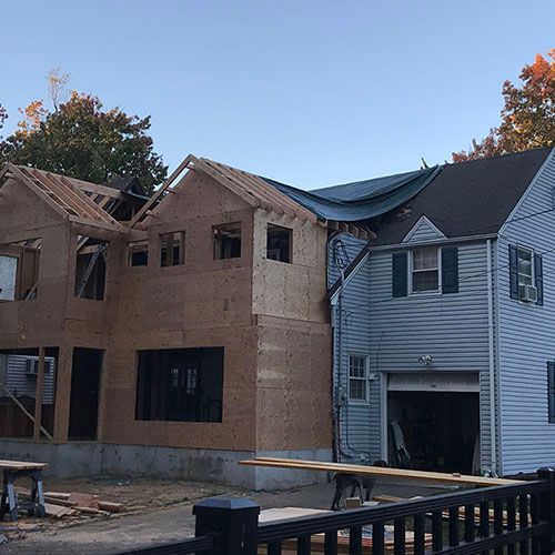 House under construction; new addition with exposed wooden framing next to an older blue house.