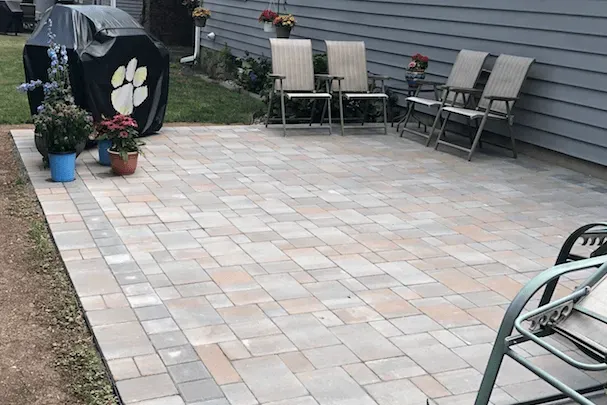 Patio paved with rectangular stones, chairs, potted plants, and covered grill.