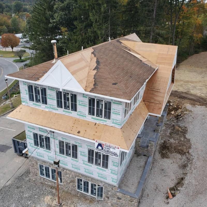 Two-story house under construction with brown roofing, white siding, and stone foundation.