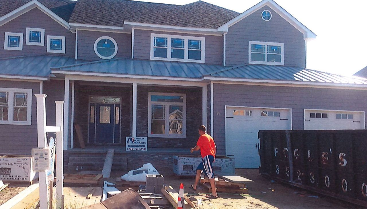 House under construction with a man working outside. Gray siding, blue door, white garage door, and a metal roof.