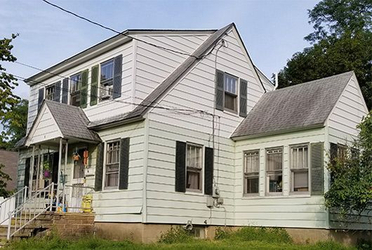 White two-story house with black shutters, a porch, and an attached sunroom on a grassy lot.