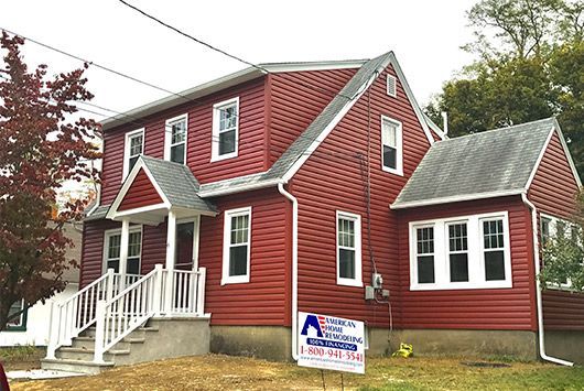 Red sided two-story house with white trim and a sign in the yard.
