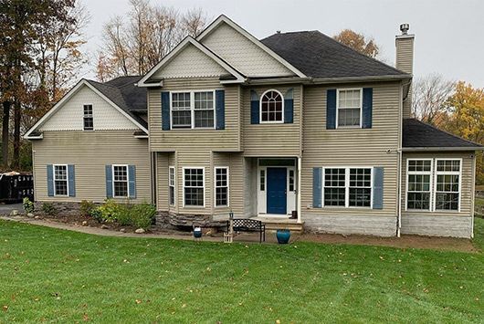 Two-story house with tan siding, blue shutters, and door, with a green lawn.