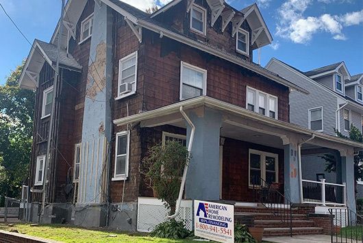 Two-story house undergoing renovation with exposed siding and a sign in front.