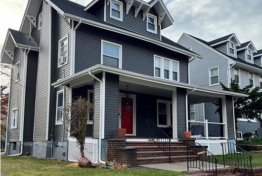 Two-story house with dark gray siding, a red front door, and a covered porch.