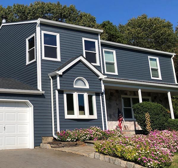 Blue-sided house with white trim, windows, and garage door, surrounded by pink flowers.