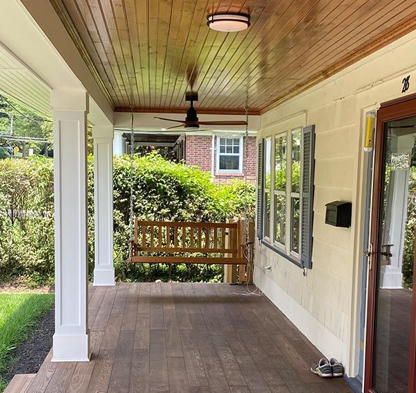 Covered porch with wood swing, columns, wood ceiling, and white walls.