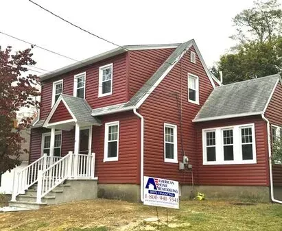 Red-sided house with white trim and a white staircase. Sign in front of the house.