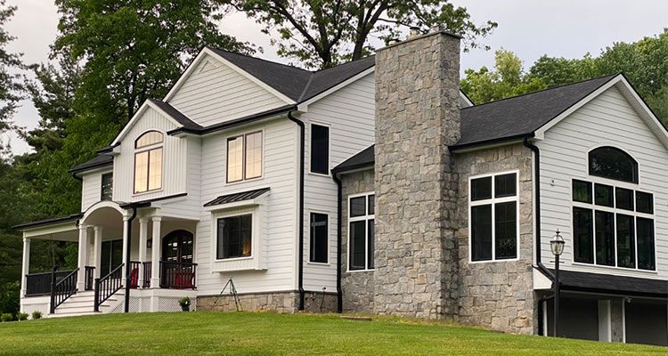 Two-story white house with black roof and stone chimney, set on a green lawn.