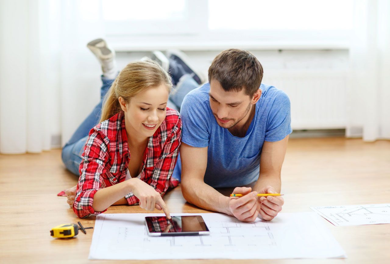 Couple lying on floor, looking at blueprints and a tablet; focused.