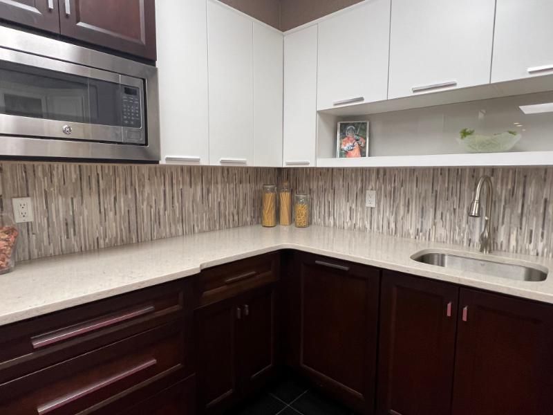 Modern kitchen with white and dark wood cabinets, stainless steel appliances, and a mosaic backsplash.