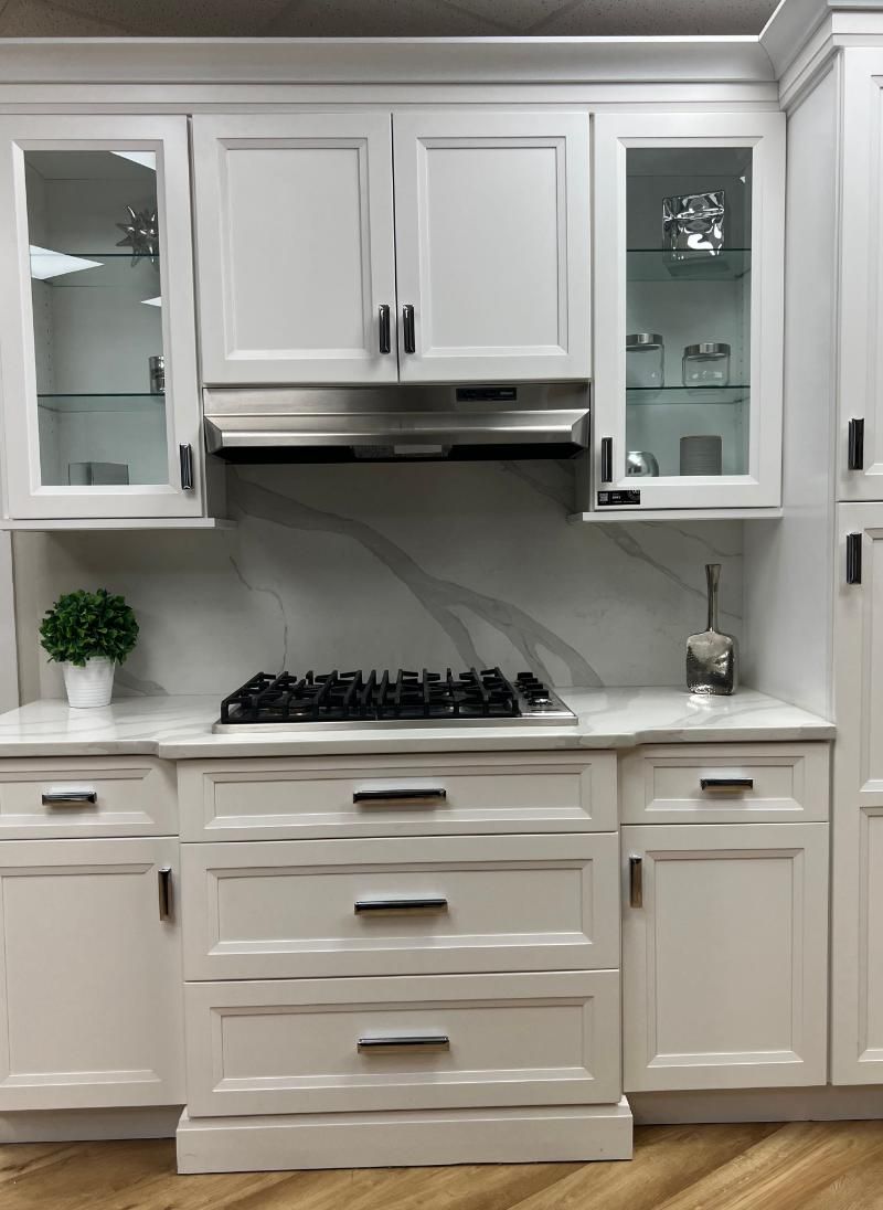 White kitchen cabinets with black hardware and a stainless steel range hood over a gas stove.