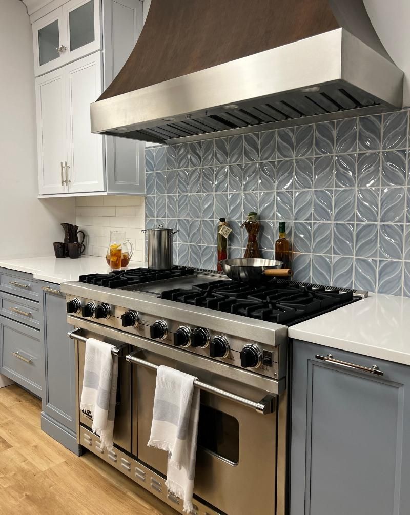 Kitchen with stainless steel range, gray cabinets, blue tile backsplash, and wood hood.