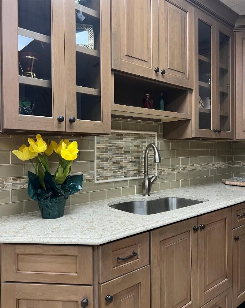 Kitchen with tan cabinets, light countertop, stainless steel sink, and yellow flowers.