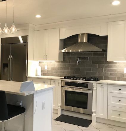 Bright kitchen with white cabinets, stainless steel appliances, and gray tile backsplash.