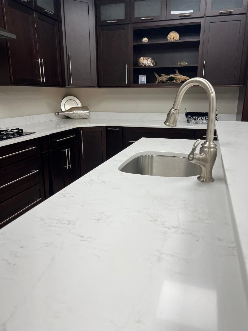 Modern kitchen with dark cabinetry, white countertops, and stainless steel sink and faucet.