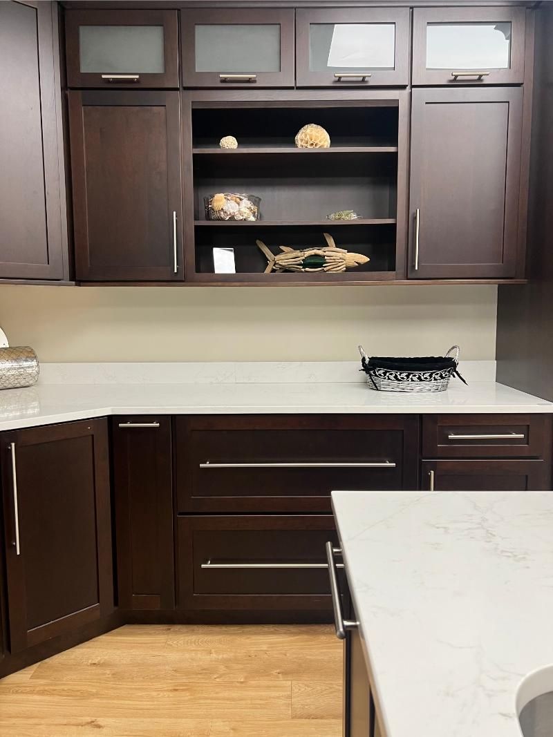 Dark wood kitchen cabinets with white countertop. Shelving displays decorative items.