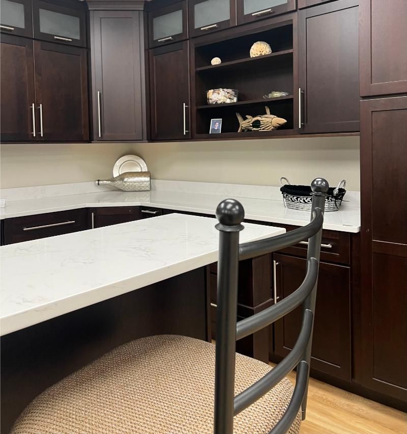 Dark wood kitchen with white countertop, chair in foreground, cabinets and shelf above.