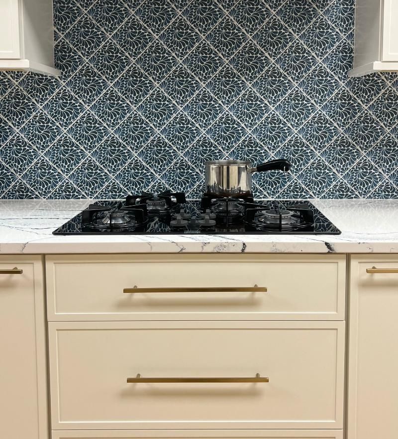 Kitchen stovetop with a pot, cream cabinets, and blue mosaic tile backsplash.
