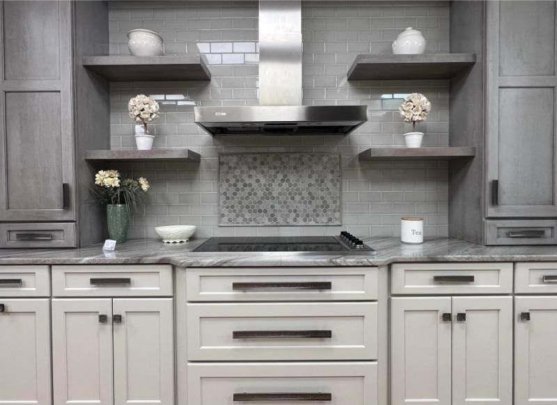 Gray and white kitchen with stove, range hood, open shelves, and cabinets.